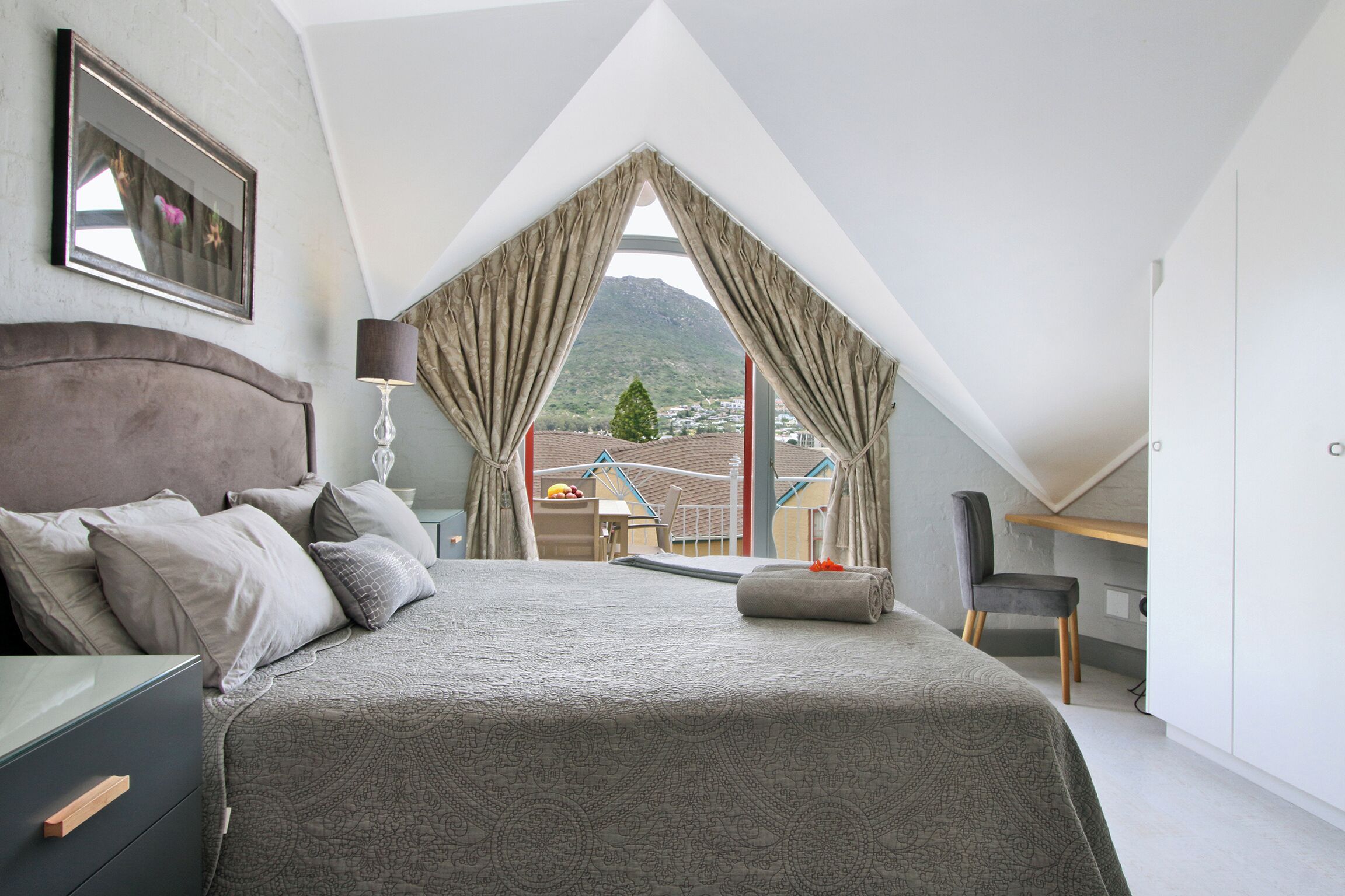 A bedroom with a large bed, a desk, and a view of a mountain.