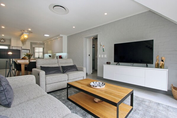 A modern living room with a grey sofa, a wooden coffee table, and a large flat-screen TV mounted on a white wall. - The Village by ITC Hospitality (Cape Town)