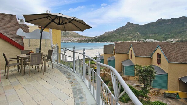 Une terrasse avec une table et des chaises, un parasol, et une vue sur la plage et les montagnes.