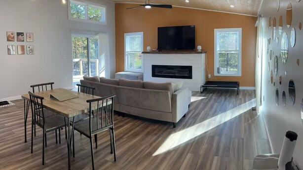 Uma sala de estar moderna com lareira, uma mesa de jantar com cadeiras, um sofá e uma televisão na parede.
