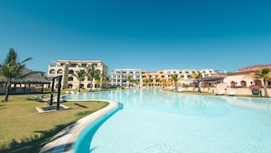 A resort pool with a curved edge, palm trees, and a building with multiple balconies in the background. - Studio 3 Guests Balcony With Views Fishing Lodge (Punta Cana)