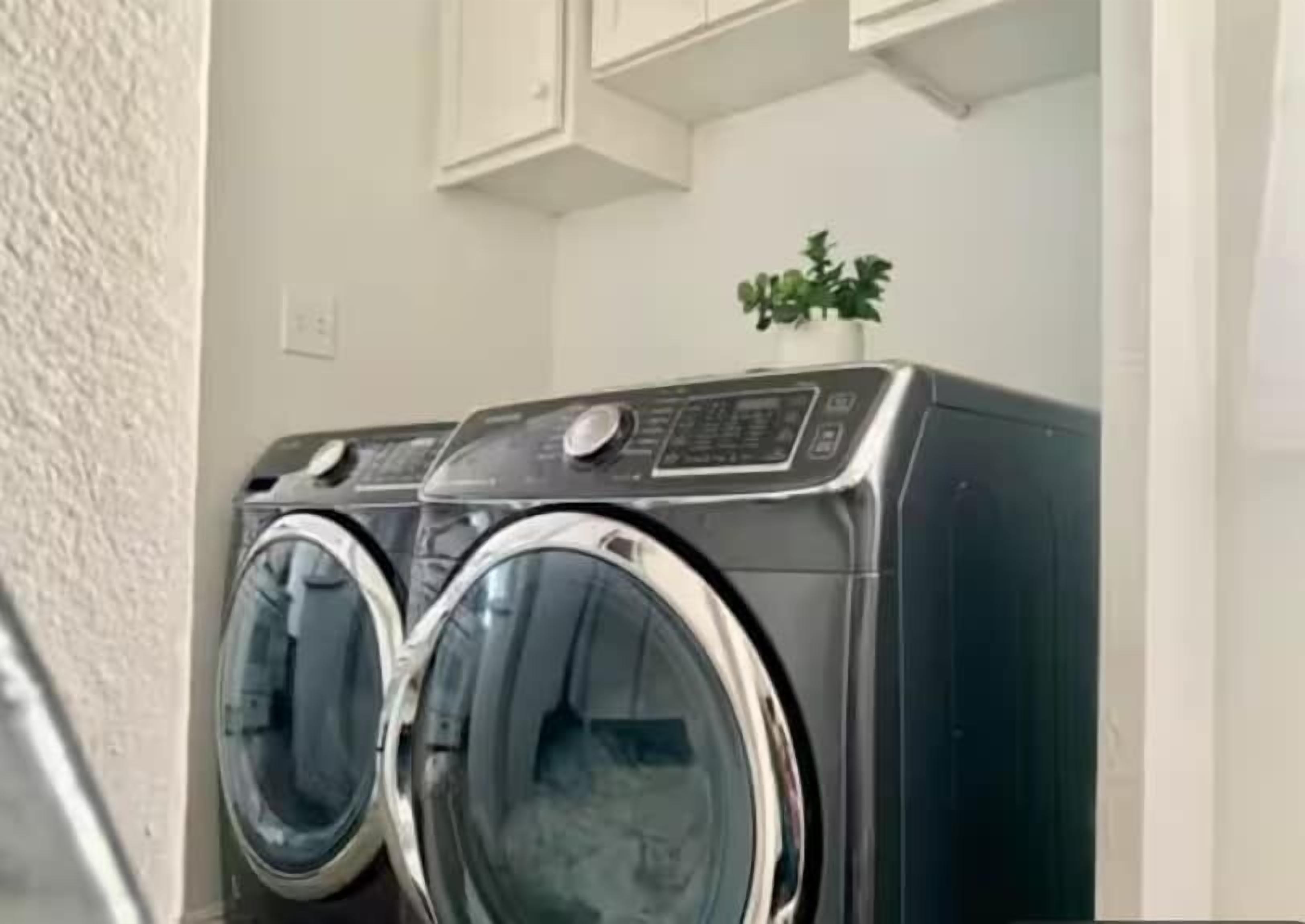 A front-loading washer and dryer in a laundry room with white cabinets above.