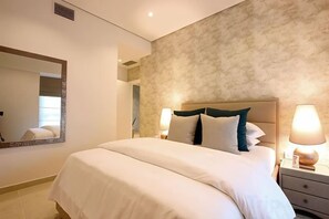 Quarto de hotel com uma cama grande, luminárias de cabeceira, mesa de cabeceira e espelho na parede.