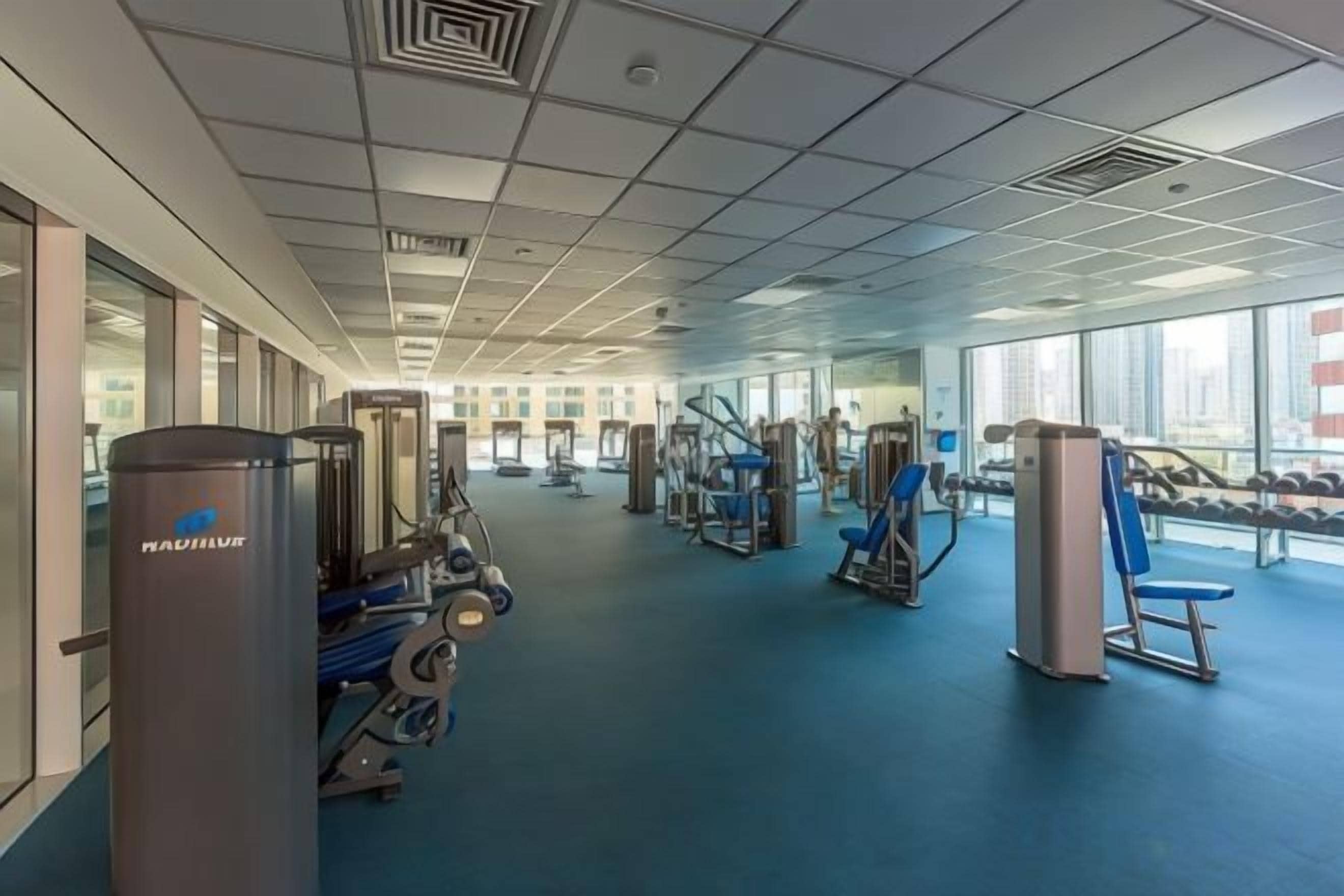 Academia com equipamentos de ginástica e amplas janelas.