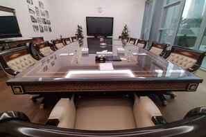 Un salón de conferencias con una mesa de vidrio, sillas de cuero, un televisor y un ventanal grande.