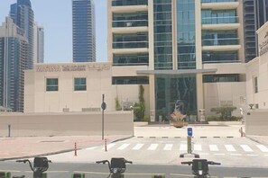 Um edifício moderno com fachada em vidro ampla, entrada destacada e área de estacionamento com vários veículos.