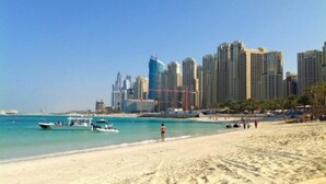 Una playa con un paisaje urbano al fondo, incluyendo rascacielos y un cielo azul despejado.