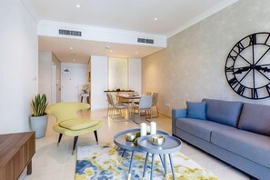 A modern living room with a sofa, armchairs, a dining area, and a large wall clock. - Marina Hotel Apartments (Dubai)