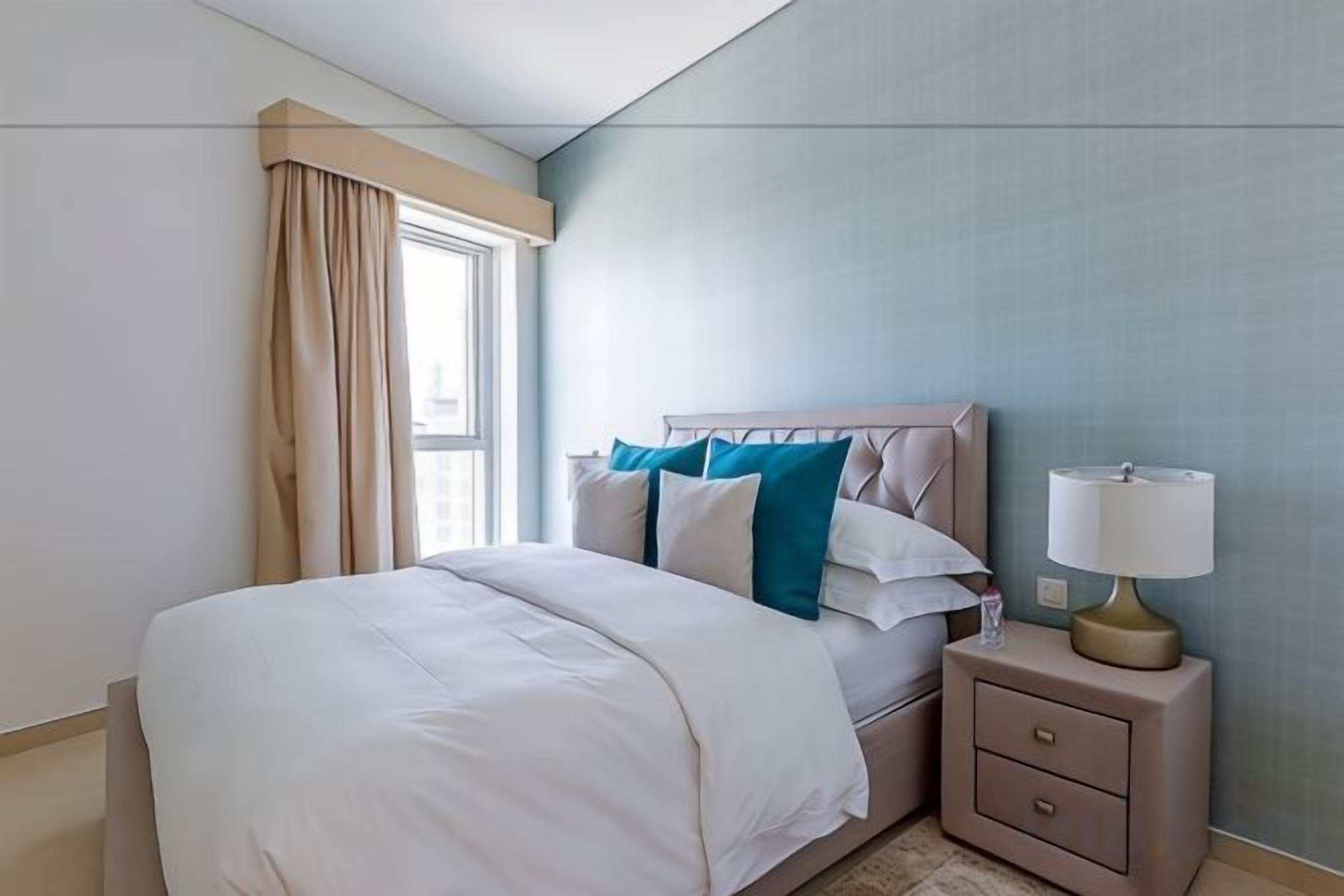 A hotel room with a bed, a nightstand, a lamp, and a window with curtains.