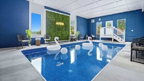 An indoor swimming pool with swan floats, a green wall with a neon sign, and a staircase leading to a balcony.