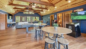 A spacious room with a wooden ceiling, a pool table, a bar area, and a television screen.
