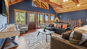 A spacious living room with a high ceiling, wooden beams, and a large window.