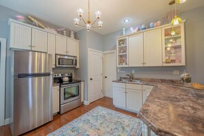 A kitchen with stainless steel appliances, white cabinetry, a granite countertop, and a chandelier. - Wizard House + Hot Tub, Private Creek, Large Yard, EV Charge (Walland)