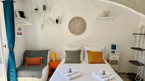 A bedroom with a bed, bedside tables, a lamp, a shelf with decorative items, and a hanging rack. - "LA PIOL" apartment in the heart of Hyères (Hyères)