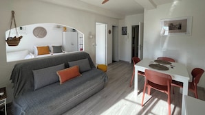 A modern living room with a grey sofa, a ceiling fan, and a dining area with a white table and red chairs. - "LA PIOL" apartment in the heart of Hyères (Hyères)
