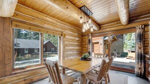 L’intérieur d’une cabane en rondins, avec une grande table à manger en bois, des chaises en bois et un luminaire suspendu.