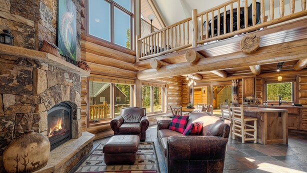 Un intérieur spacieux de chalet en bois, avec une cheminée en pierre, des meubles en cuir et un grand espace dédié à la salle à manger.