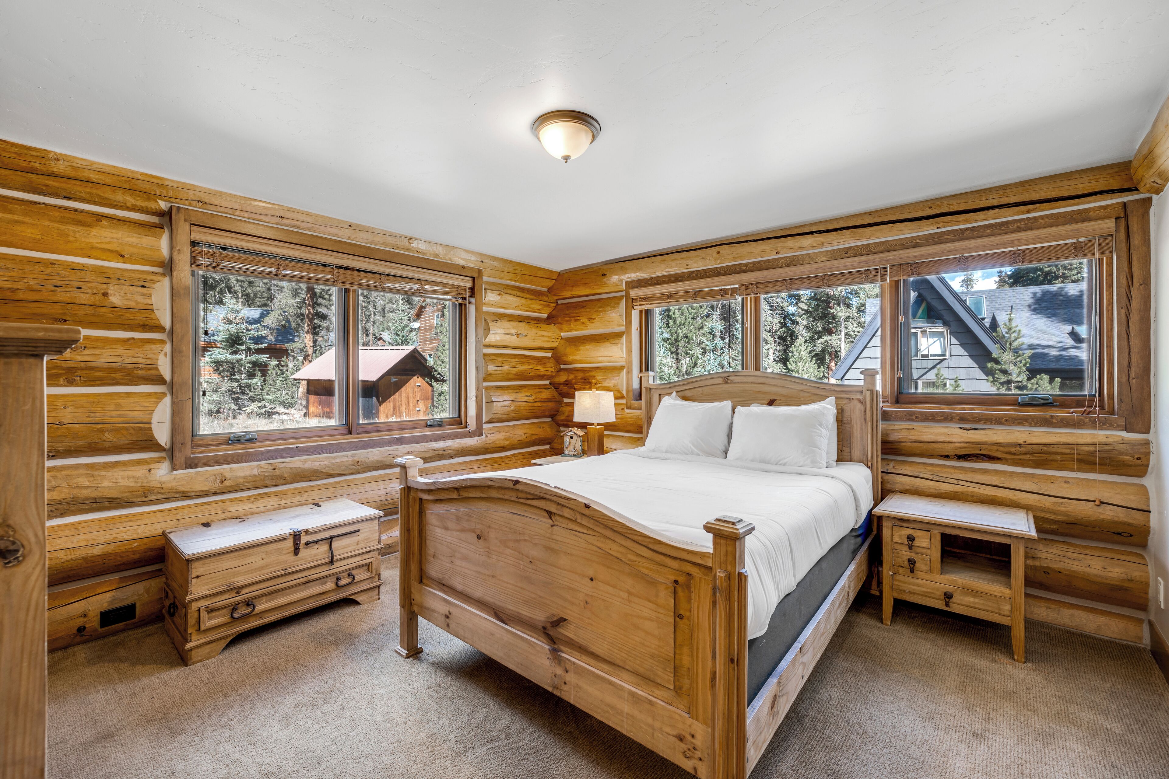 Een slaapkamer in een blokhut met een houten bed, twee nachtkastjes en grote ramen met uitzicht op het omliggende bos.