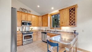 Una cocina con armarios de madera, electrodomésticos de acero inoxidable, encimera de granito y ventana con vistas a árboles.