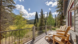 Una terraza de madera con mobiliario exterior y vistas a un valle boscoso.