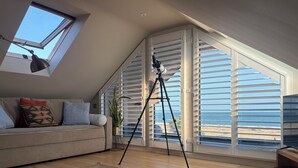 Una sala de estar acogedora con techo alto, tragaluz, un trípode y vista a la playa.