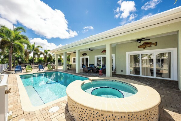 A swimming pool with a hot tub, lounge chairs, and palm trees.