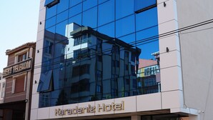 Um hotel moderno com fachada de vidro refletivo, entrada com tapete vermelho e vasos de madeira na frente.