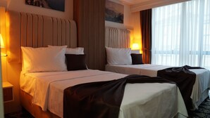 Quarto de hotel com duas camas, cada uma com cabeceira, abajures e vista para o exterior através de grandes janelas.