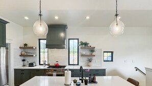 Een moderne keuken met een groot eiland, donkere kastjes en hanglampen.