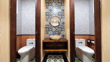 Une salle de bain avec deux toilettes, un lavabo avec un miroir et des carreaux décoratifs aux murs et sur le sol.