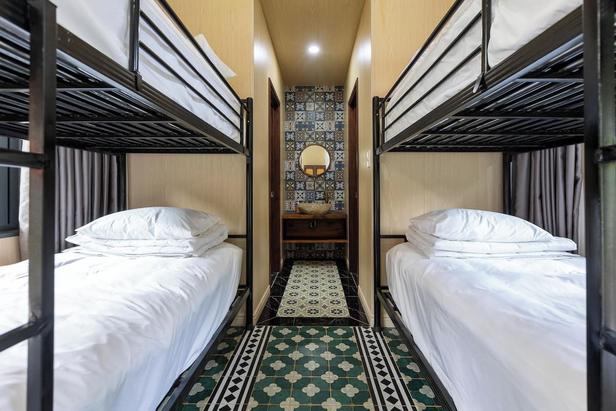 A narrow corridor with bunk beds on either side, a patterned floor, and a mirror on the wall.