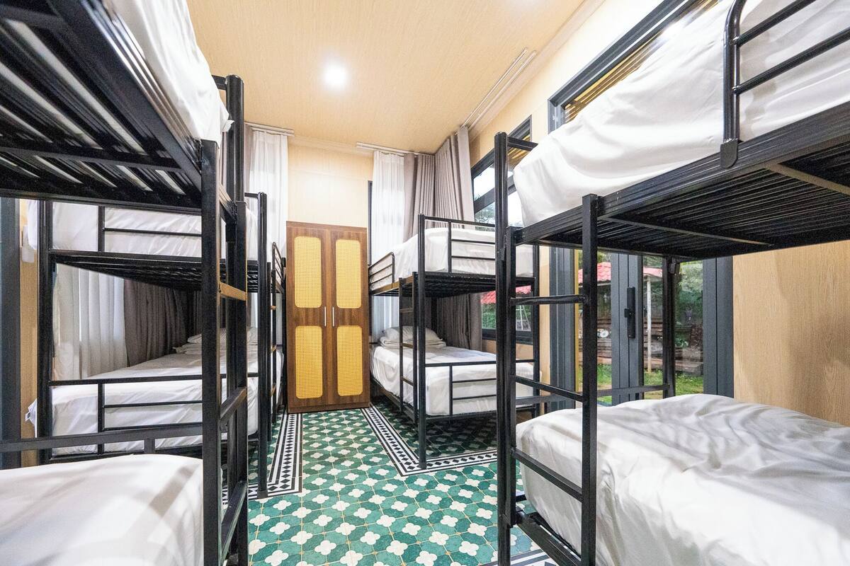 A dormitory room with bunk beds, a patterned floor, and a wooden door.