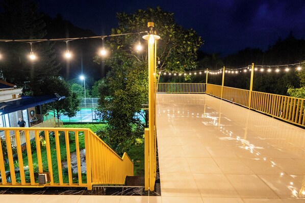 A well-lit outdoor area with a yellow railing, a paved walkway, and string lights.