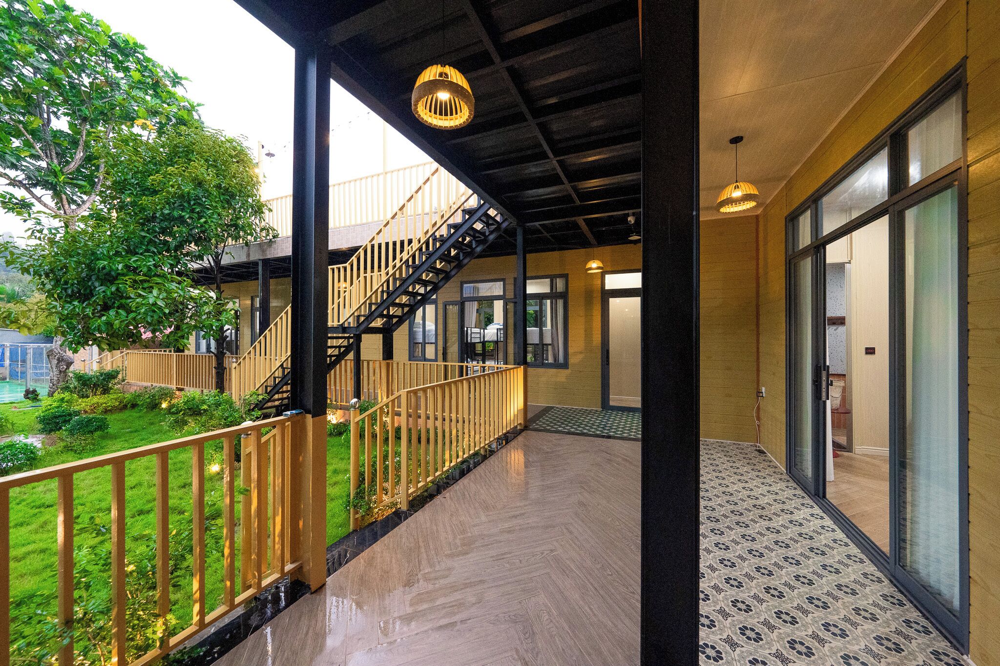 Un espacio exterior cubierto con una escalera de madera que sube a un nivel superior, una entrada con puerta de cristal y un suelo estampado.