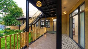 Un espacio exterior cubierto con una escalera de madera que sube a un nivel superior, una entrada con puerta de cristal y un suelo estampado.
