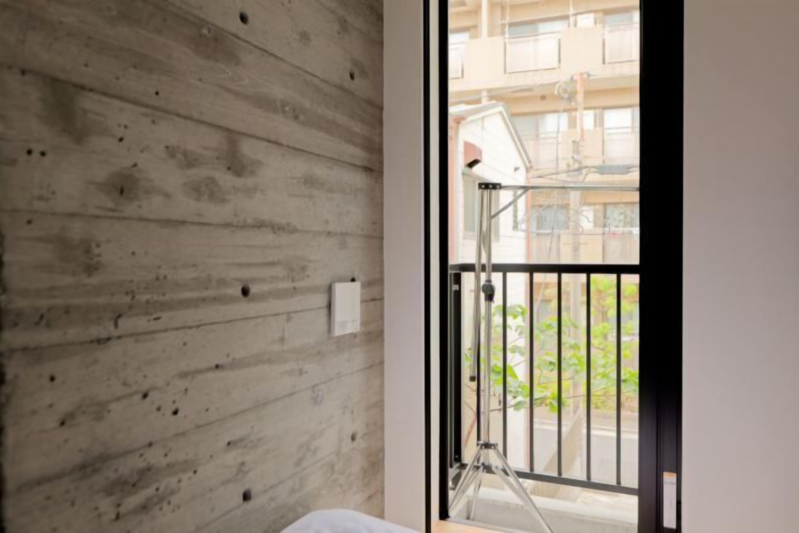 A room with a concrete wall, a window with a metal gate, and a visible balcony. - Calm Riverside Inn/Close to Ikebukuro (Tokyo)