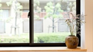 A window with a view of a garden and a vase with flowers on a windowsill. - Calm Riverside Inn/Close to Ikebukuro (Tokyo)