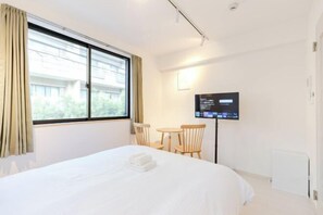 A hotel room with a bed, a desk, a chair, a TV, and a window with curtains. - Calm Riverside Inn/Close to Ikebukuro (Tokyo)