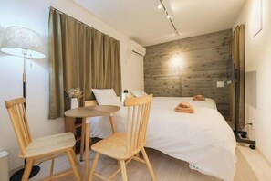 A hotel room with a bed, two wooden chairs, a small round table, a lamp, and a wooden wall panel. - Calm Riverside Inn/Close to Ikebukuro (Tokyo)