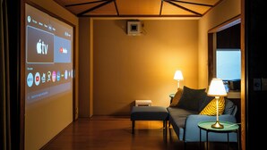 A hotel room with a bed, a small table with a lamp, a projector screen displaying app icons, and a wooden ceiling. - Ikkenyahotel FUKUOKA (Fukuoka)