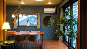 A dining area with a wooden table, four chairs, a hanging light fixture, and a potted plant. - Ikkenyahotel FUKUOKA (Fukuoka)