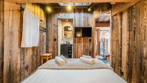 Ein Zimmer aus Holz mit einem Bett, einem kleinen Tisch, einem Spiegel und einem Fernseher.