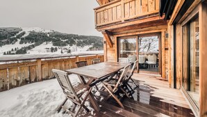 Eine Holzterrasse mit Tisch und Stühlen, mit Blick auf eine verschneite Landschaft aus Bäumen und Hügeln.