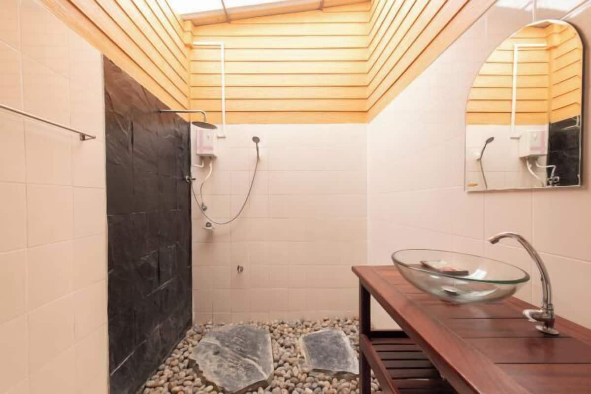 A bathroom with a wooden slatted ceiling, a glass bowl sink, and a tiled floor with stepping stones.