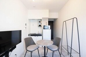A compact living space with a flat-screen TV, a small round table, two chairs, a kitchenette, and a black metal shelf. - Sumida DIAS (Tokyo)