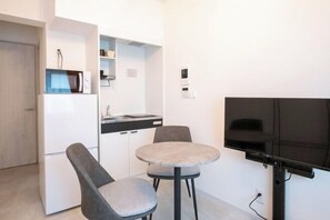 A compact kitchen with a microwave, a small dining table with two chairs, and a flat-screen TV mounted on the wall. - Sumida DIAS (Tokyo)