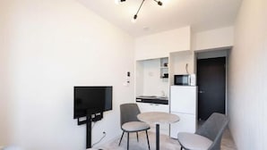 A modern living room with a flat-screen TV, two grey armchairs, a round coffee table, and a sofa with cushions. - Sumida DIAS (Tokyo)