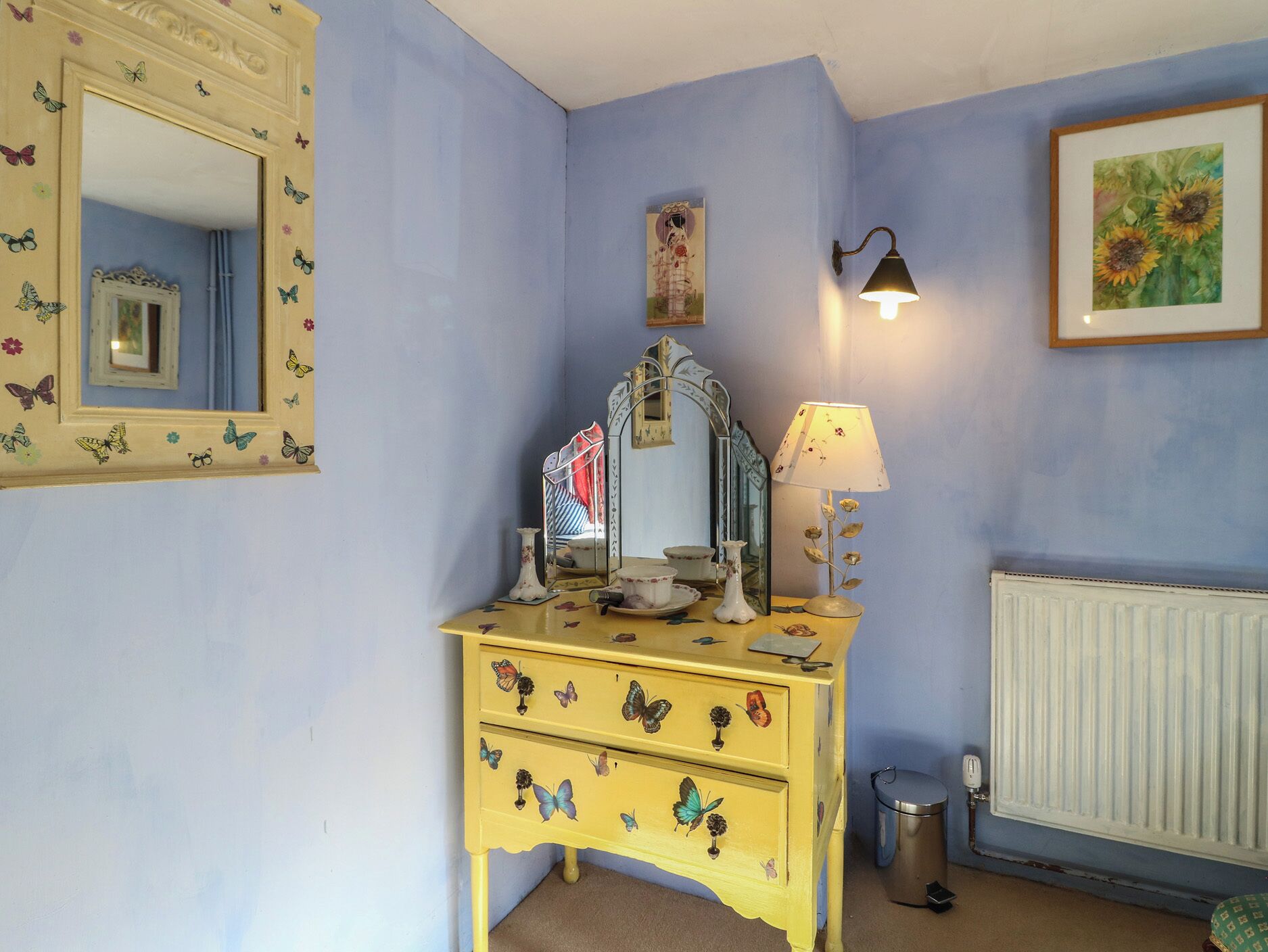 A room with a yellow dresser, a mirror, a wall-mounted lamp, and a radiator.