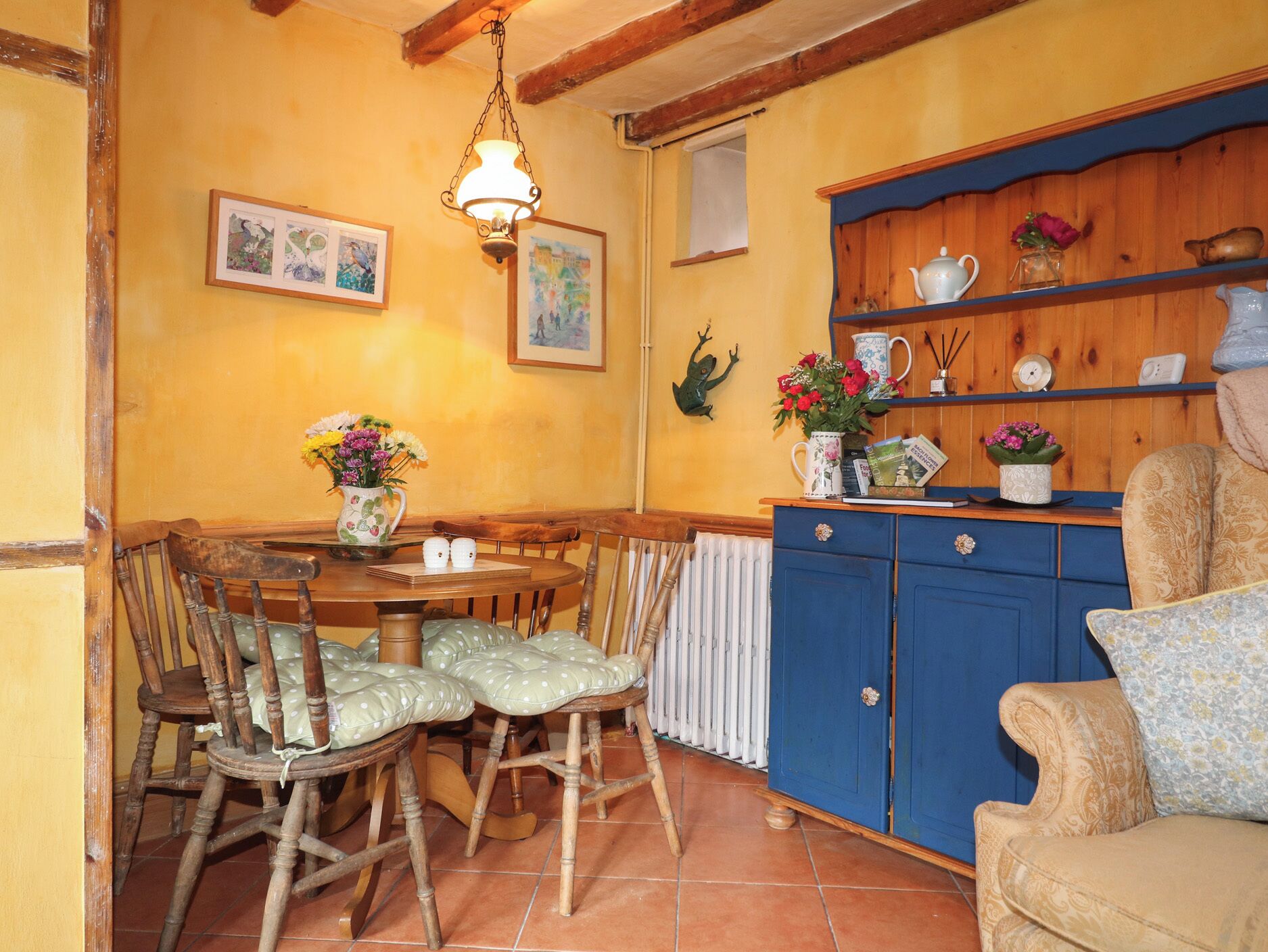 A dining area with a wooden table and chairs, a blue cabinet with decorative items, and a hanging light fixture.