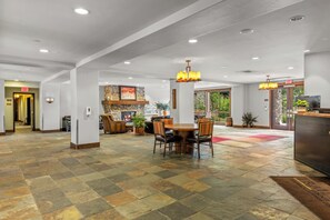 A spacious lobby with a stone-tiled floor, a central seating area with a round table and chairs, a stone fireplace, and a modern chandelier. - Modern 2BR Retreat w/ Pool & Gondola 1088 (Steamboat springs)